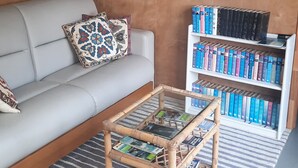 A living room with a sofa, a coffee table with magazines, a bookshelf with books, and two framed artworks on the walls. - Kingfisher Cabin. Nestled Pukekohe side of Bombay, with a large private pool. (Bombay)