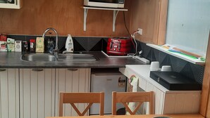 A compact kitchen with a microwave, toaster, and sink. There is a wooden dining table with chairs. - Kingfisher Cabin. Nestled Pukekohe side of Bombay, with a large private pool. (Bombay)