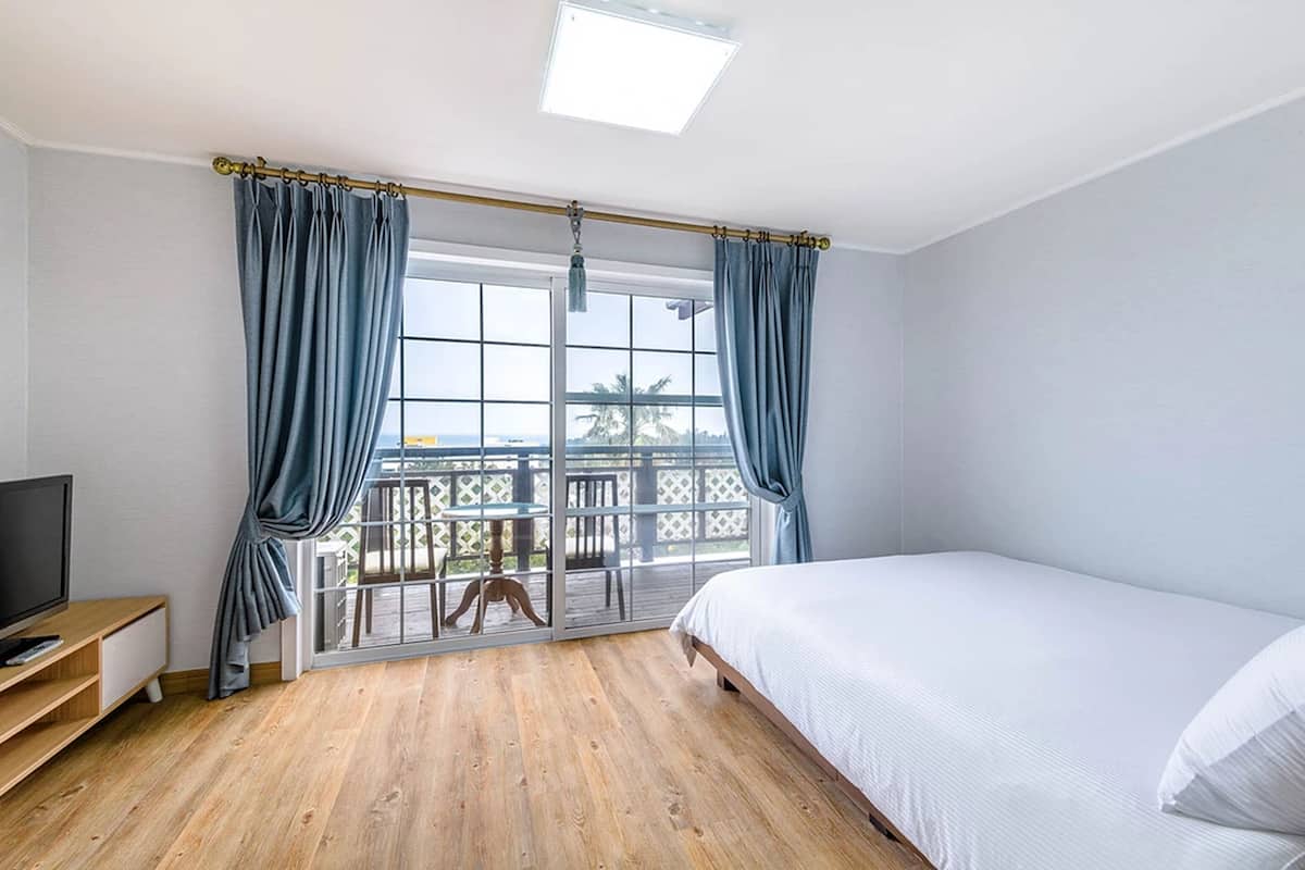 A bedroom with a bed, a TV, a wooden floor, and a balcony with a view.