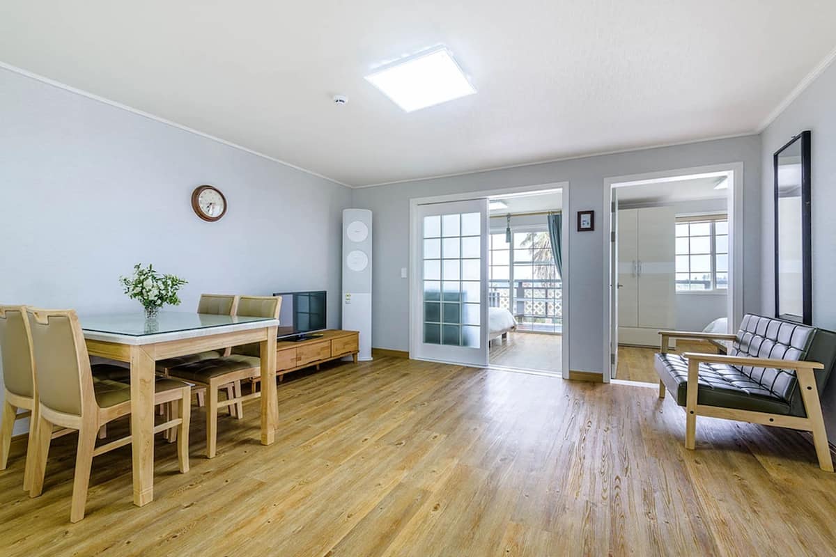 A spacious room with a wooden dining table, chairs, a sofa, and a large window.