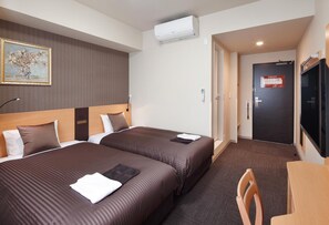 Ett hotellrum med två sängar, ett skrivbord, en stol, en luftkonditioneringsanläggning och en dörr med en skylt.