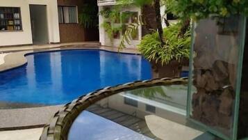 A swimming pool with a glass viewing area, surrounded by potted plants and a building with balconies.