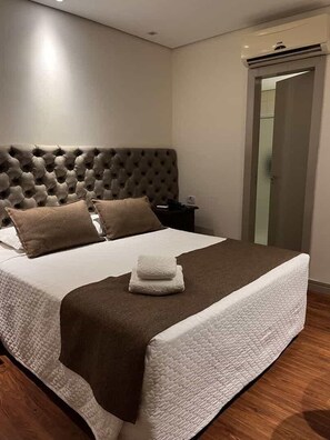 Una cama bien tendida con un cabecero capitonado, una mesita de noche y un aire acondicionado de pared.