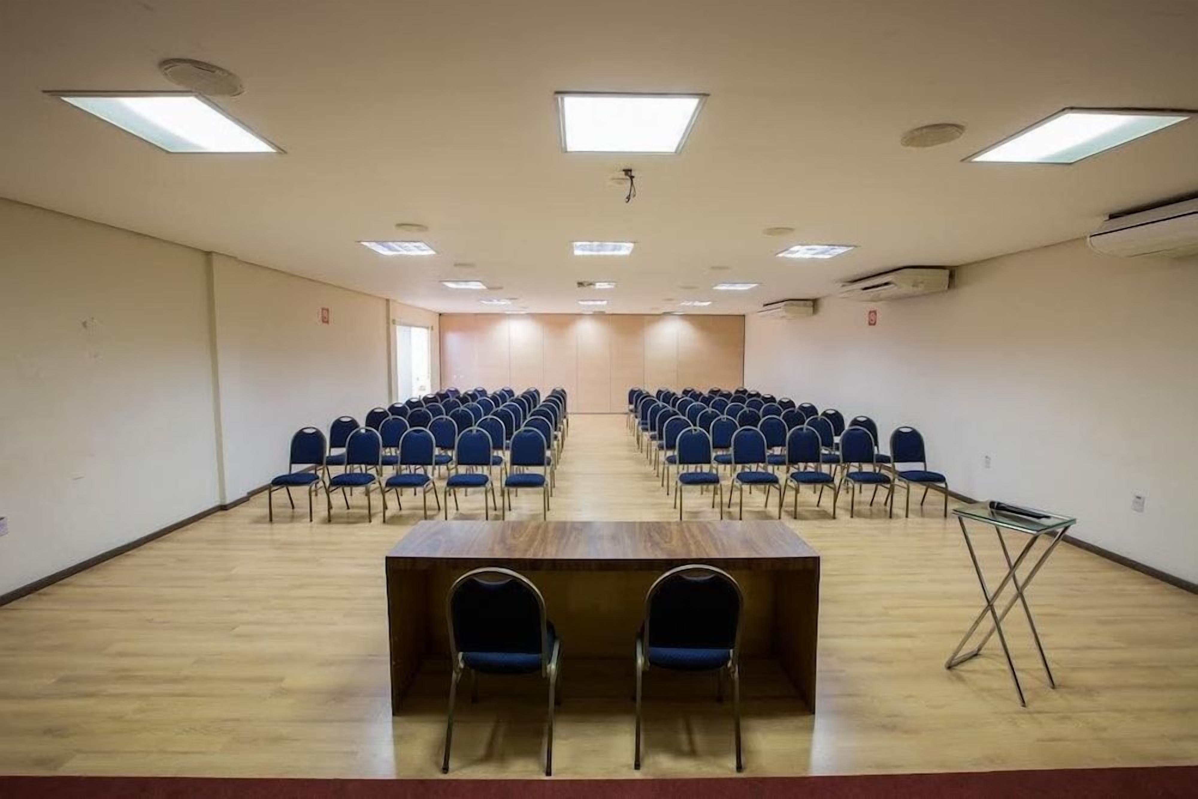 A conference room with rows of chairs, a long table, and ceiling lights.