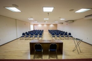 Un salón de conferencias con filas de sillas, una mesa larga e iluminación en el techo.