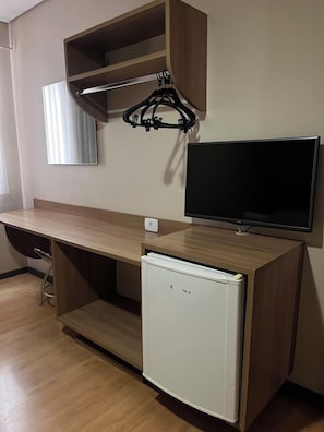 A compact room with a wooden desk, a television, and a small refrigerator. - Maximus Hoteis (JI PARANA)