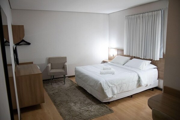 A modern bedroom with a bed, a chair, a desk, and a window with curtains.