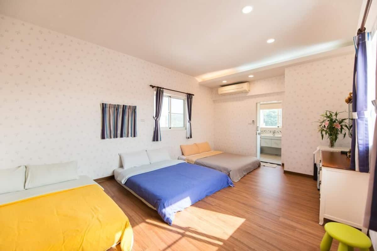 A hotel room with two beds, a small table, a stool, and a window with curtains.