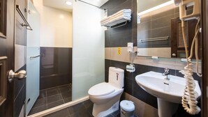 Un baño moderno con cabina de ducha de vidrio, inodoro blanco, lavamanos con teléfono y toallero.