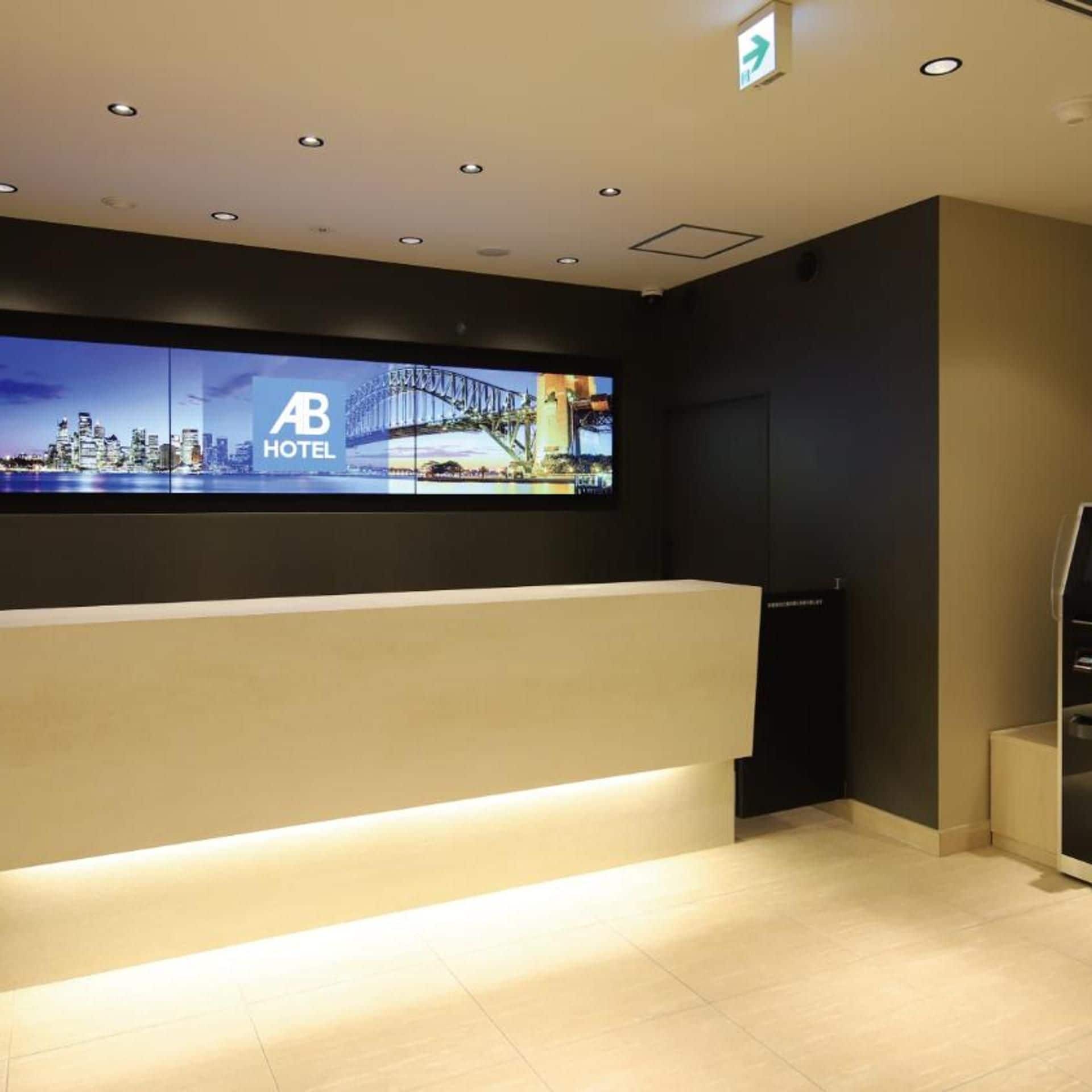 Een hotel receptiebalie met een groot scherm waarop een stadsbeeld en het logo van het hotel worden getoond.