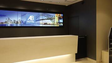 Een hotel receptiebalie met een groot scherm waarop een stadsbeeld en het logo van het hotel worden getoond.
