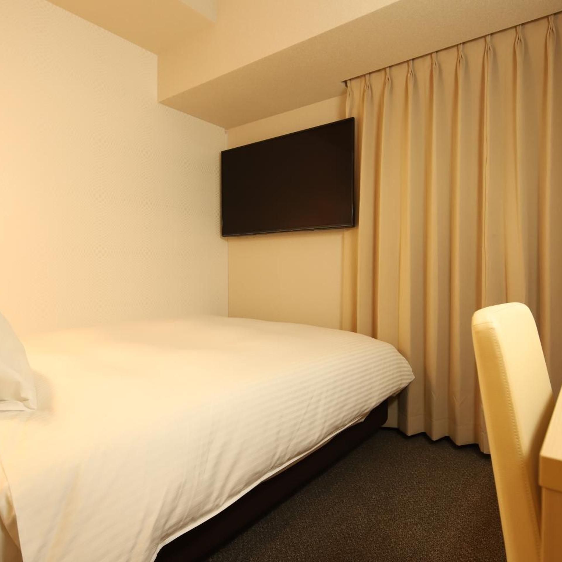 A hotel room with a single bed, a flat-screen TV mounted on the wall, and a chair.