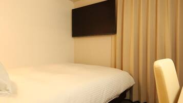 A hotel room with a single bed, a flat-screen TV mounted on the wall, and a chair.