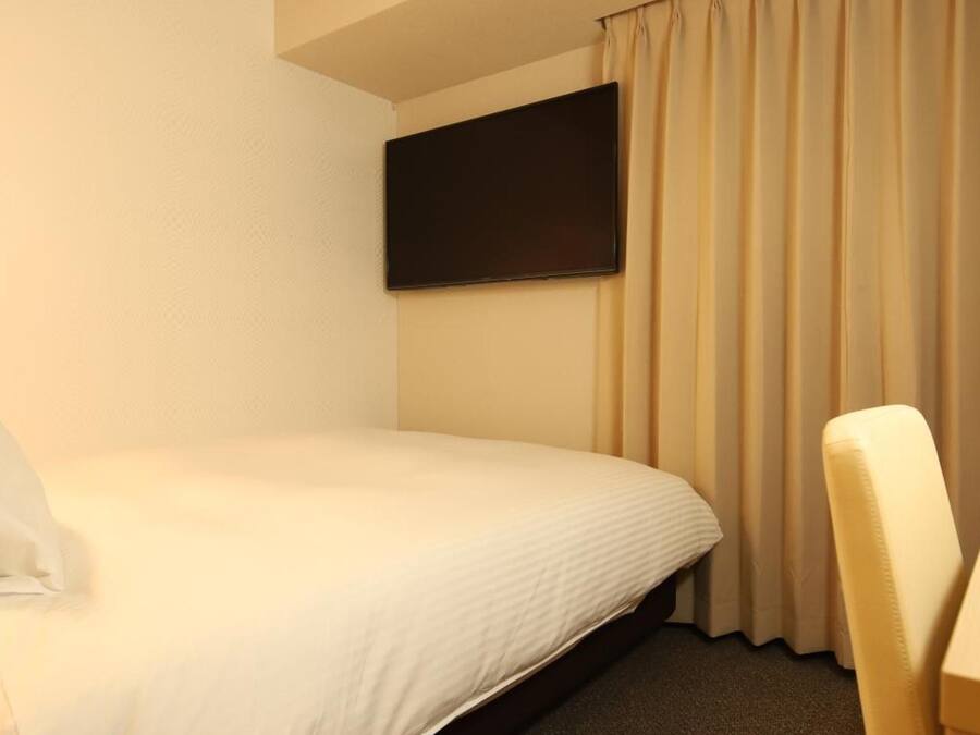 A hotel room with a single bed, a flat-screen TV mounted on the wall, and a chair.