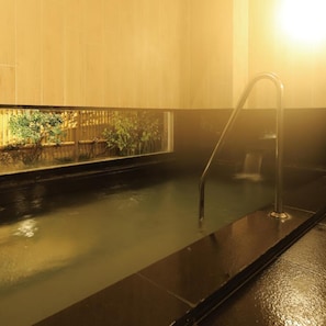 A hot tub with a metal faucet, surrounded by a wooden wall with a window.