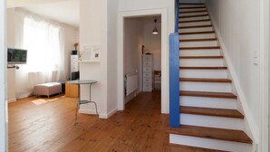 Een ruime kamer met houten vloeren, een trap met blauwe accenten en een klein tafeltje met een stoel.