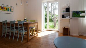 Een eetruimte met een houten tafel en stoelen, een aan de muur bevestigde televisie en een schuifdeur naar een buitenruimte.