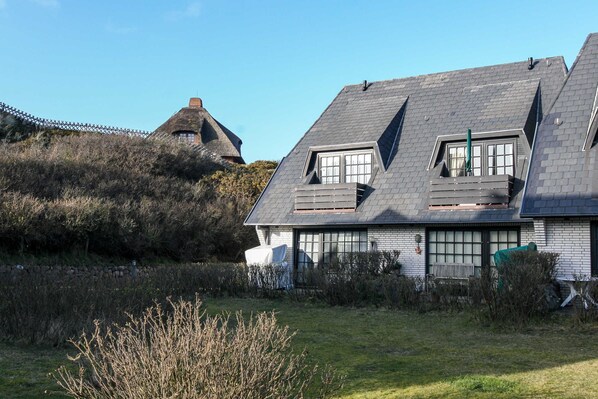 A house with a sloped roof, large windows, and a thatched roof structure in the background.