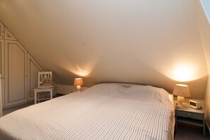 A bedroom with a bed, two bedside lamps, a chair, a small table, and a wardrobe.