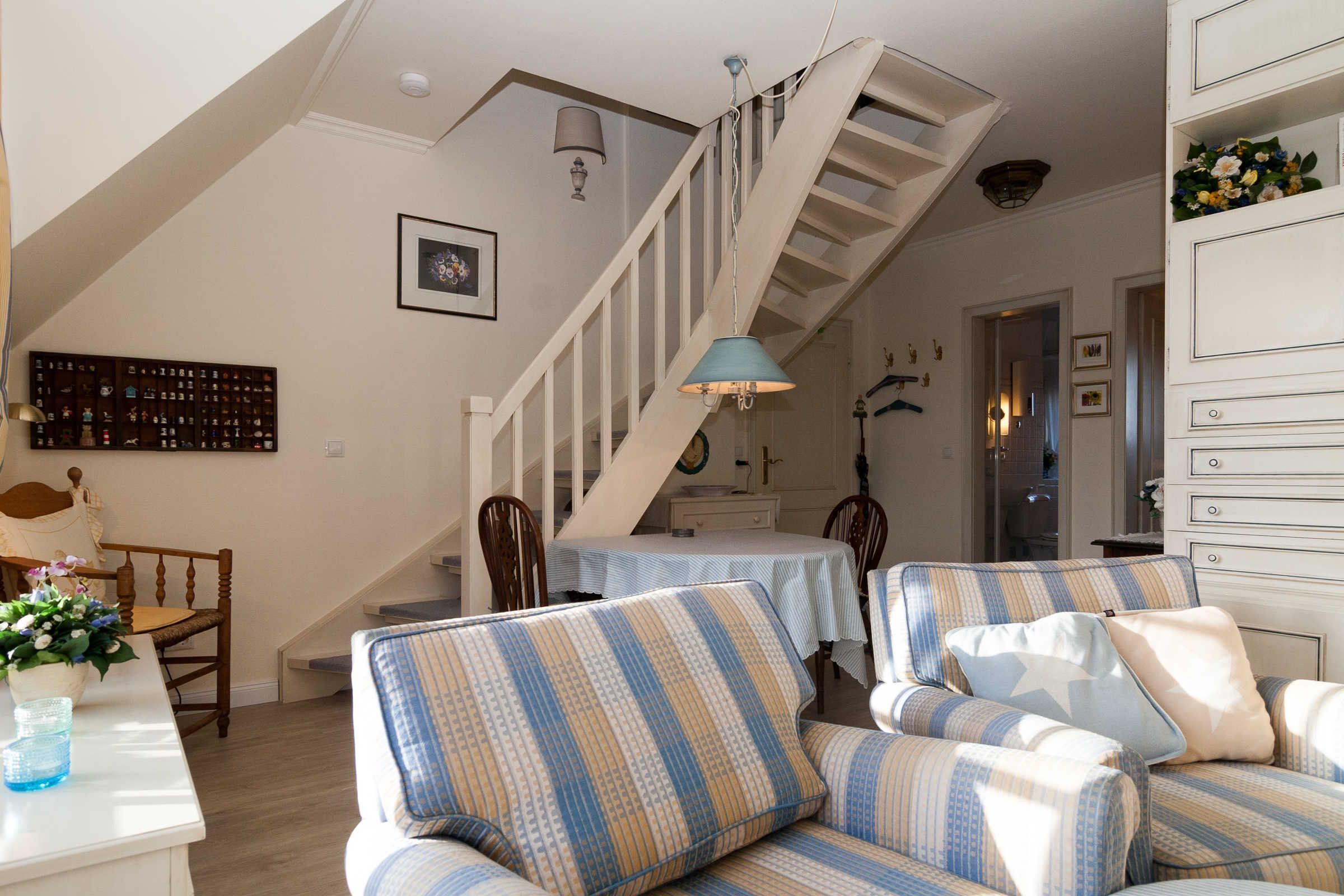 Un salon avec des canapés à rayures, un escalier et un coin repas comprenant une table et des chaises.