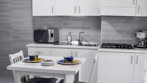 A modern kitchen with white cabinets, a microwave, a sink, and a stove. There is a dining table with chairs and a few dishes on it. - B&B Audafra (Crotone)