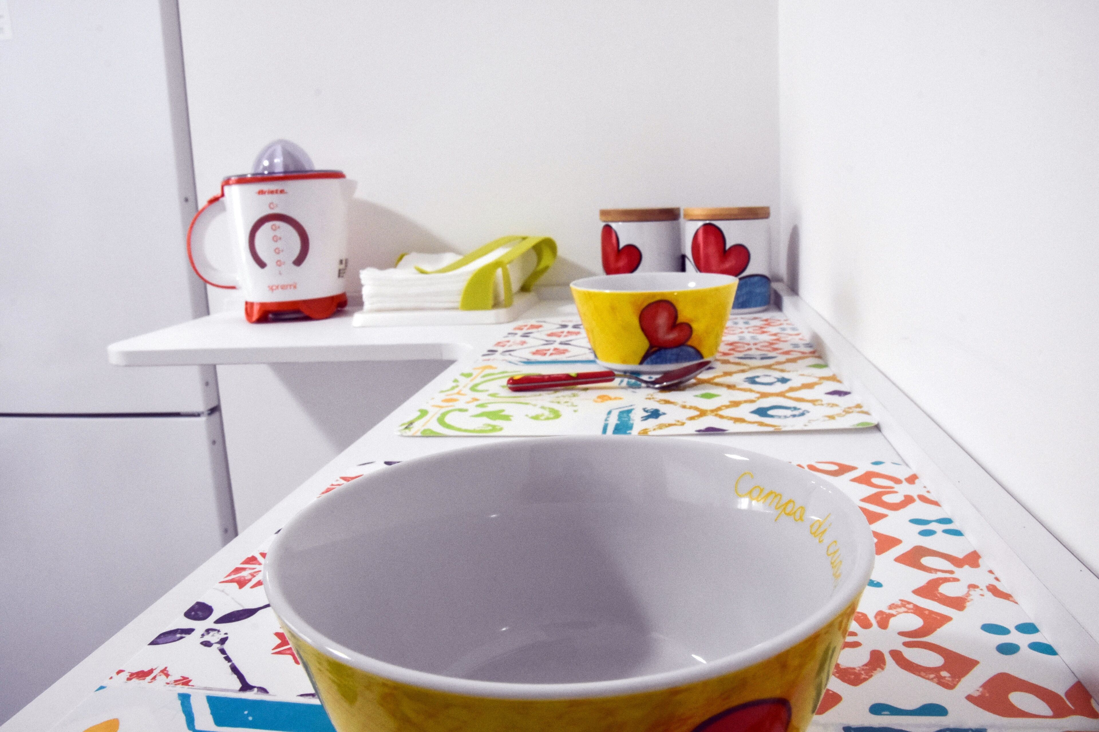 Un comptoir de cuisine avec une machine à café, une tasse jaune ornée d’un motif en forme de cœur et un bol blanc.