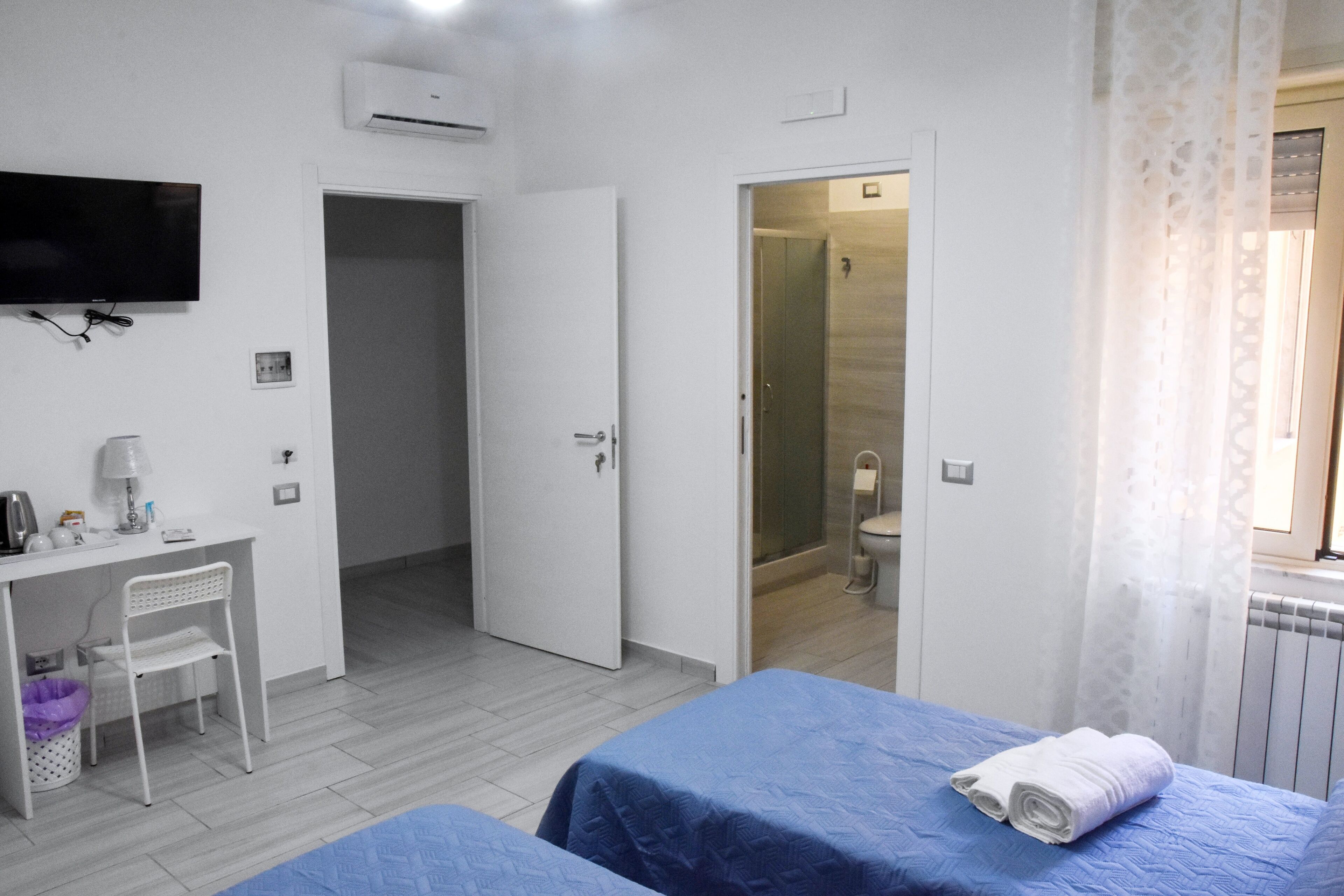 A hotel room with a bed, a desk, a chair, a TV, and a bathroom visible through an open door.