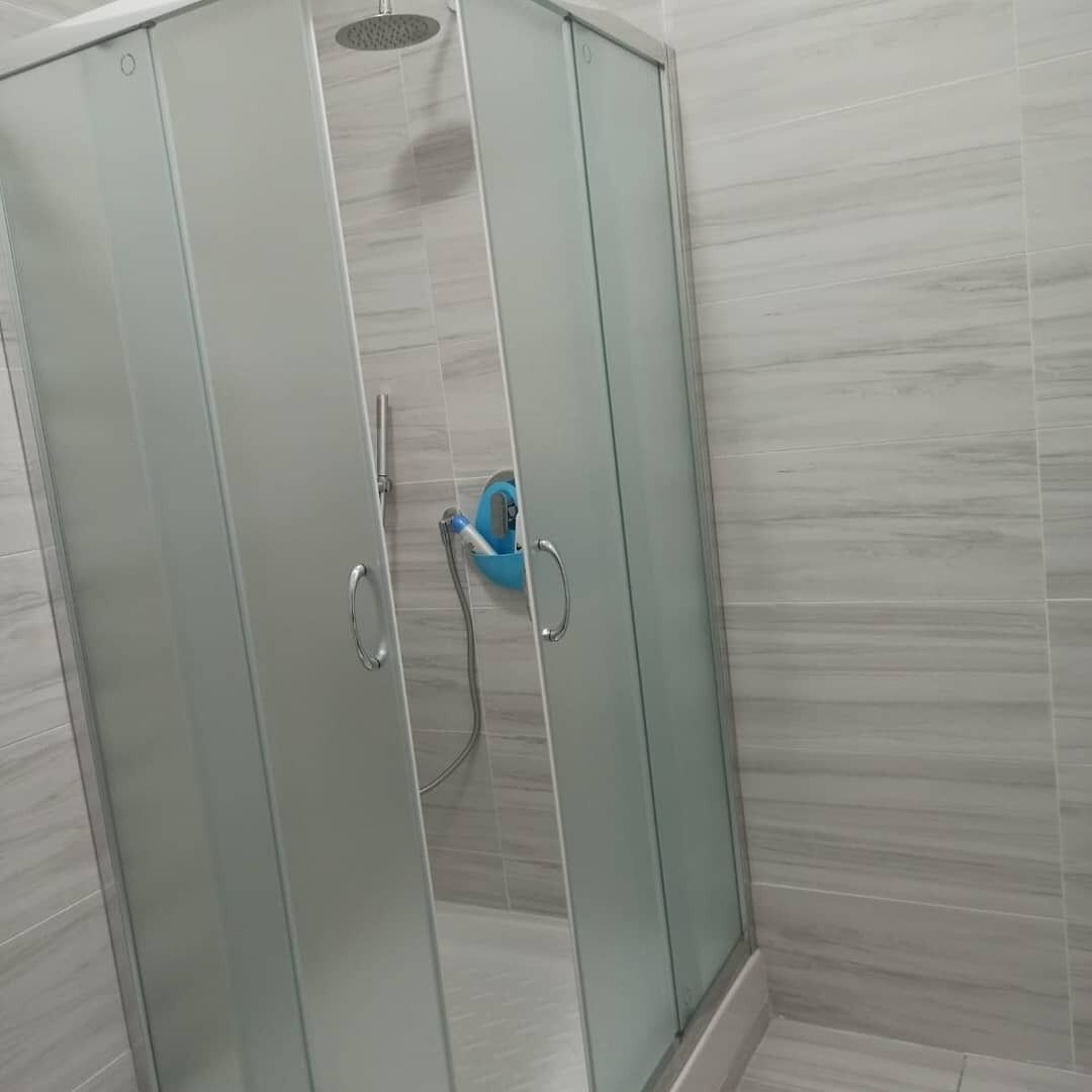 Une douche en verre avec un pommeau de douche amovible et une bouteille de shampoing bleue.