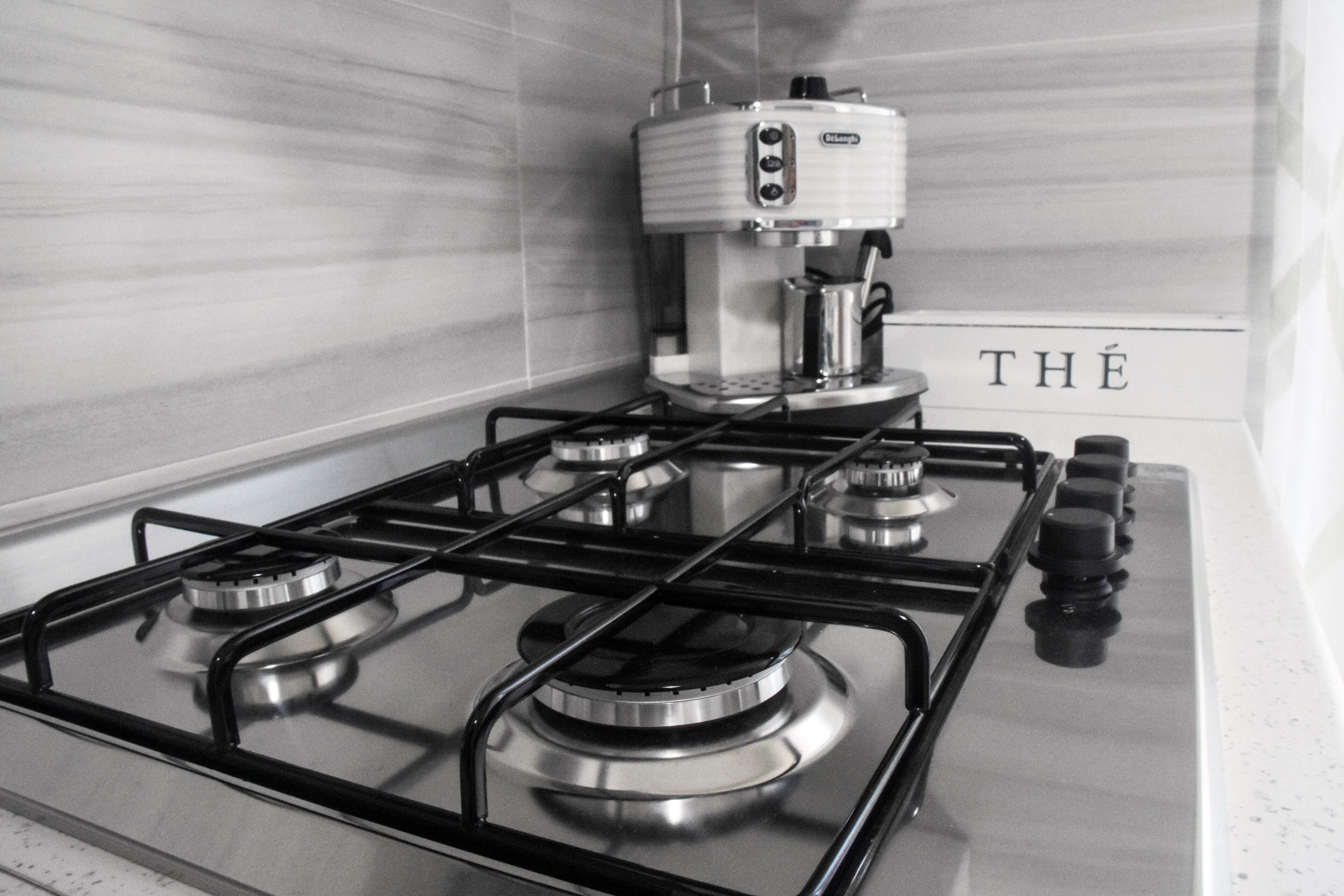 Une cuisine équipée d’une cuisinière à gaz, d’une machine à café et d’une pancarte sur laquelle on peut lire « THÉ ».