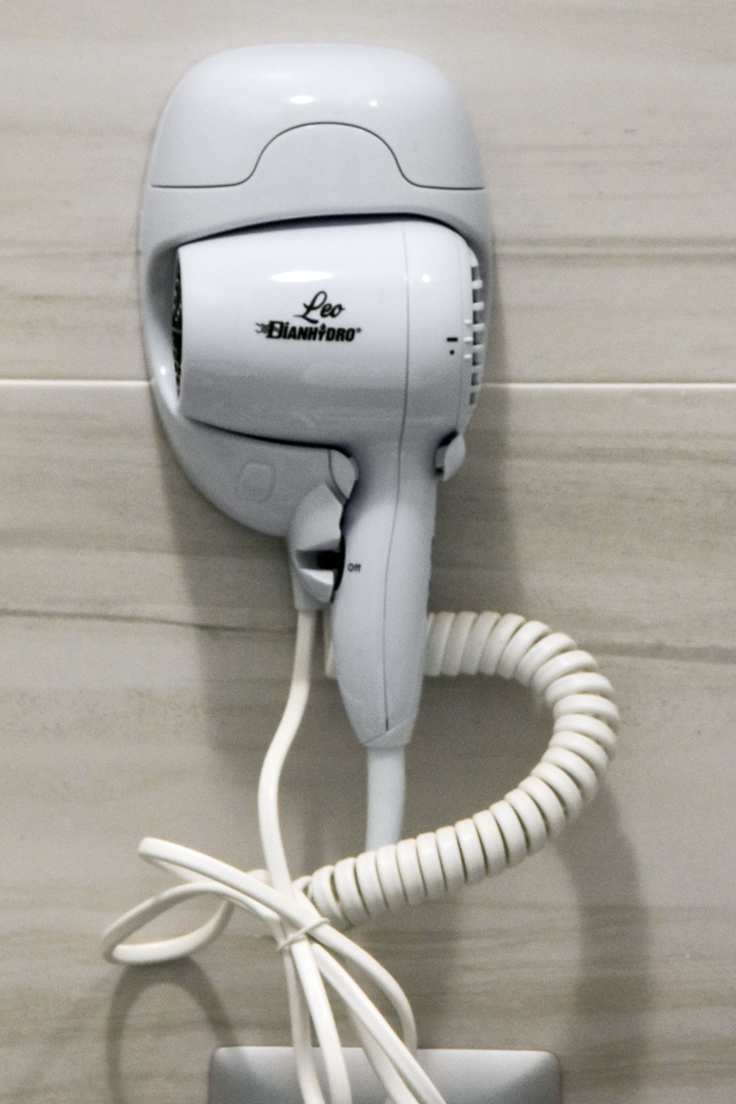A white hair dryer mounted on a tiled wall.