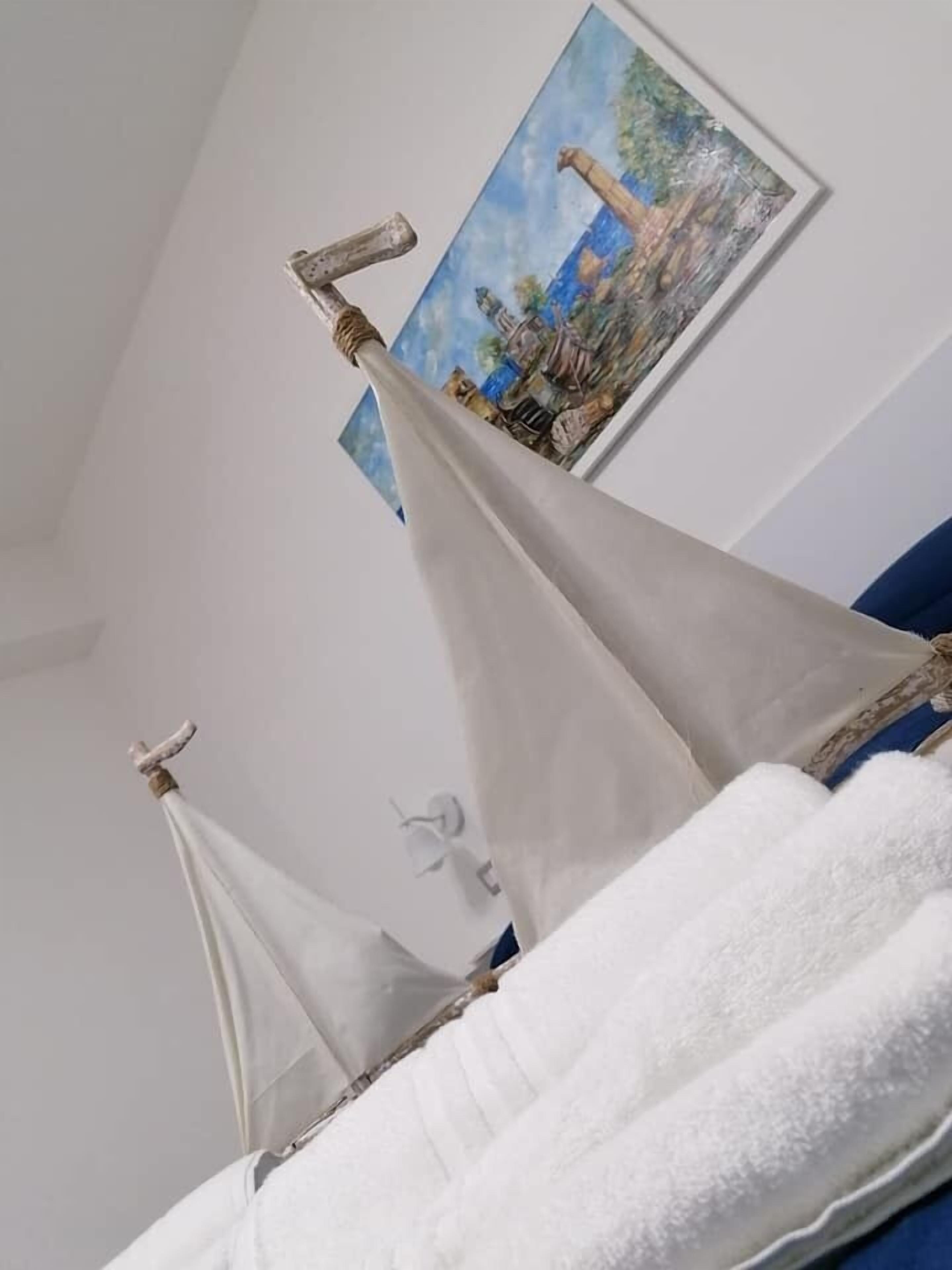 Un modelo de velero sobre una cama con un cuadro de un paisaje al fondo.