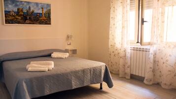 Een slaapkamer met een bed, een schilderij aan de muur, een raam met gordijnen en een radiator.