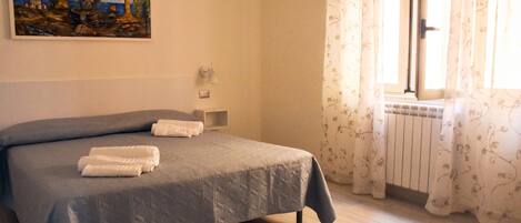 A bedroom with a bed, a painting on the wall, a window with curtains, and a radiator.
