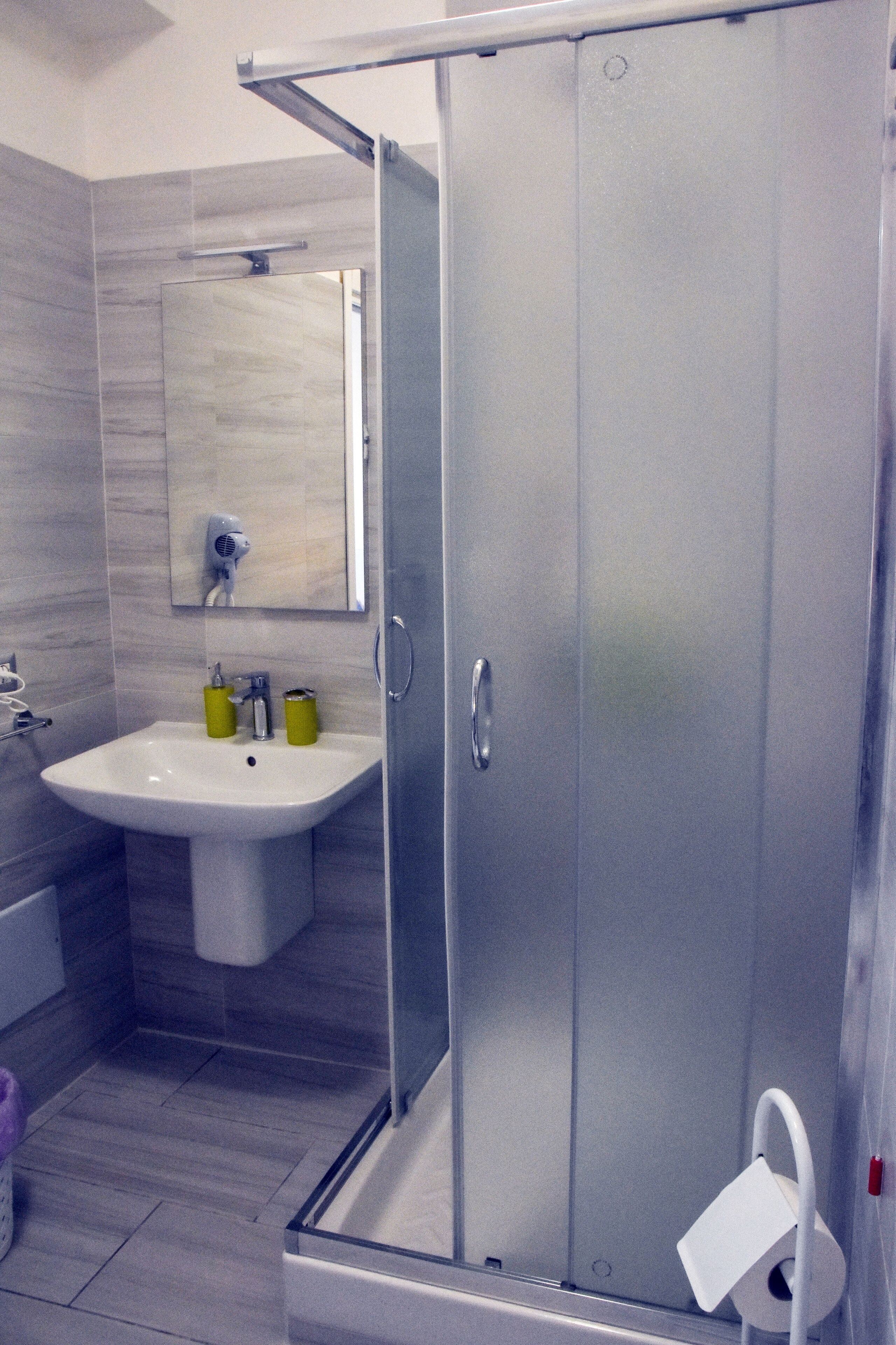 Ein modernes Badezimmer mit Duschkabine aus Glas, einem Waschbecken mit gelben Seifenspendern und einem Spiegel über dem Waschbecken.