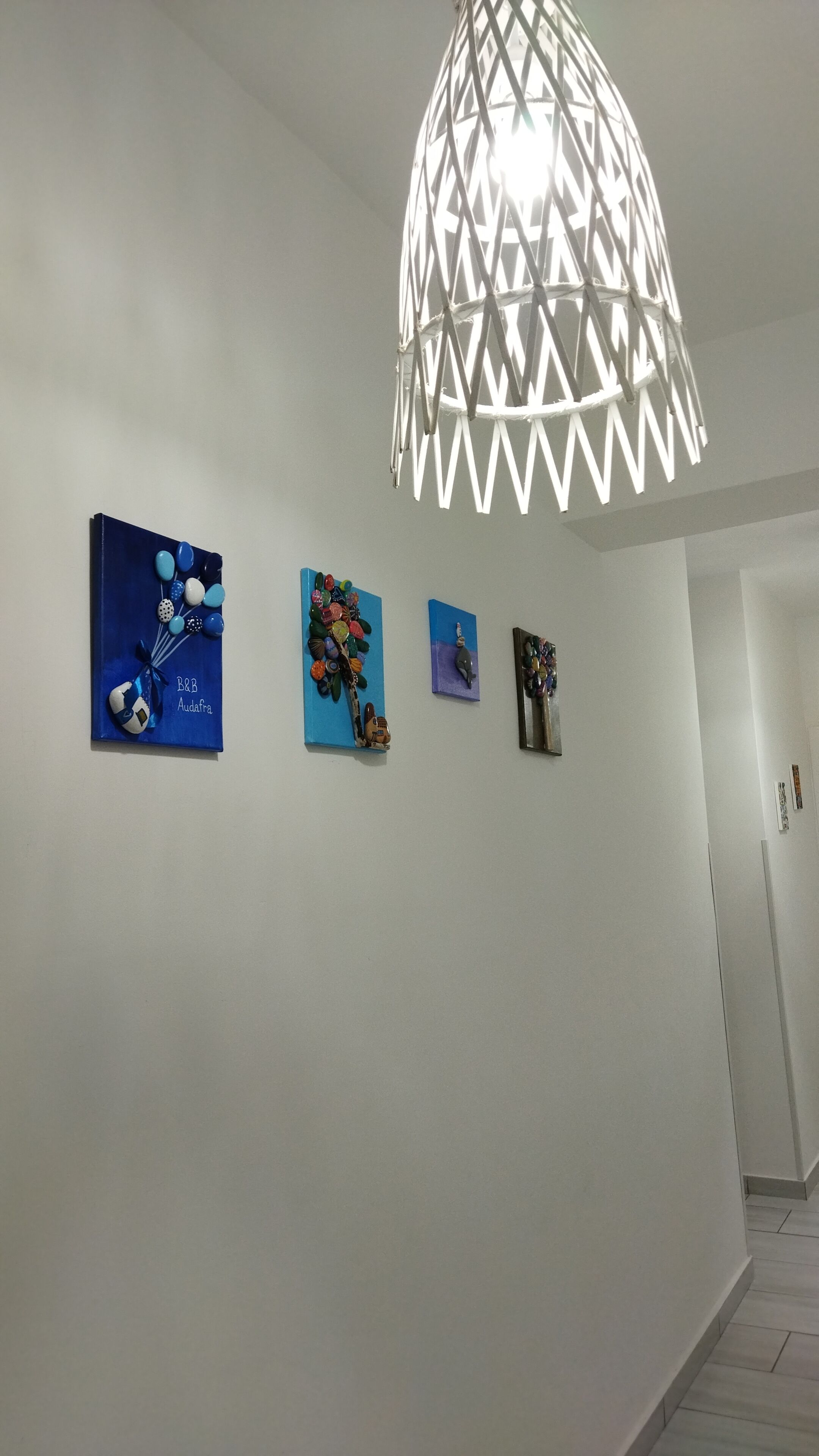 A hallway with a white wall and a hanging light fixture. There are four framed artworks on the wall.