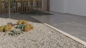 Un edificio moderno con techo plano, cerca de madera y jardín de grava con plantas.