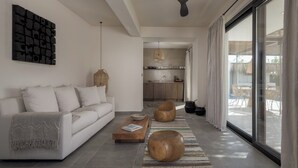 Una sala de estar moderna con un sofá, una mesa de centro y taburetes redondos de madera. Se ve una cocina al fondo.