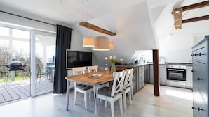 Cozinha moderna com mesa de jantar de madeira, cadeiras brancas e forno embutido.