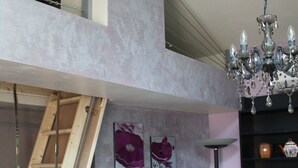 Une pièce de style « loft », avec un plafond haut, un lustre, une télévision et des œuvres d’art accrochées aux murs.