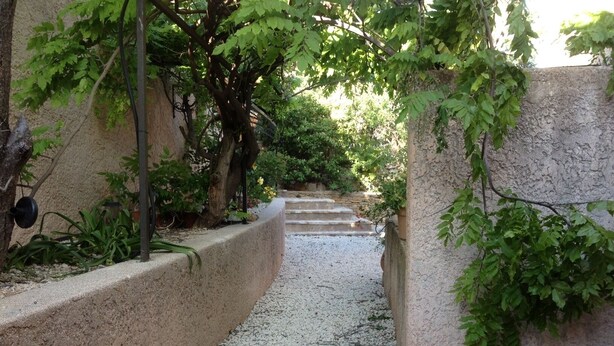 Un étroit sentier bordé de murs et de verdure, qui mène à un escalier.