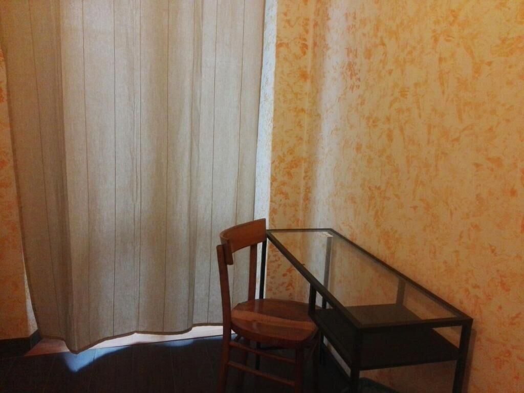 A corner room with a wooden chair, a glass table, and a curtain.