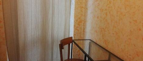 A corner room with a wooden chair, a glass table, and a curtain.