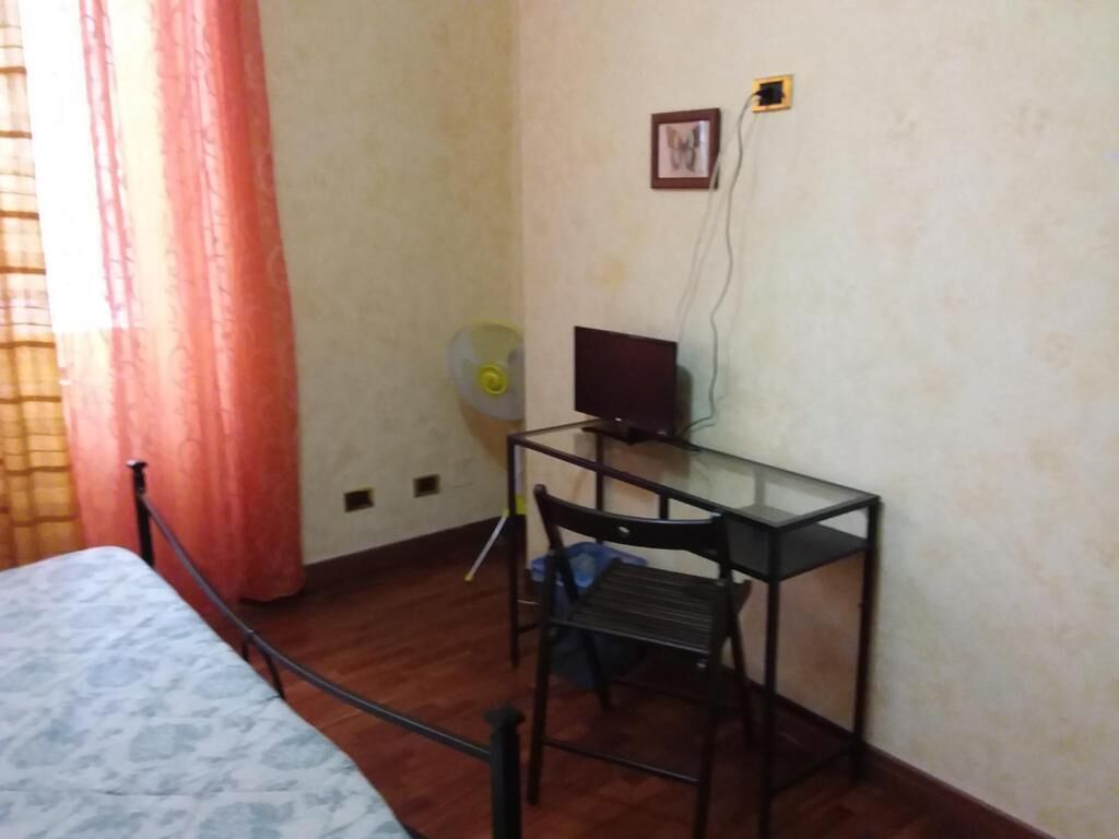 A room with a bed, a desk with a computer, a chair, and a fan.