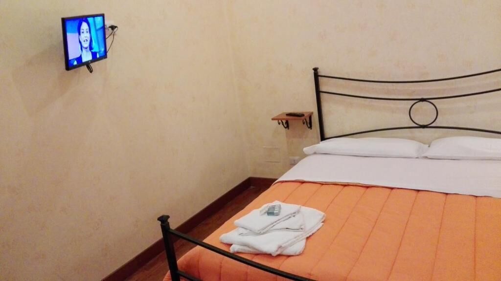 A hotel room with a bed, a TV mounted on the wall, and a small shelf.