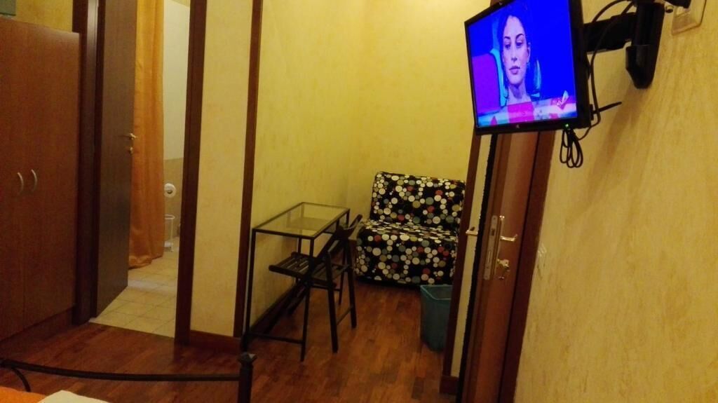 Una habitación pequeña con suelo de madera, una silla de estampado de lunares, una mesa de vidrio y un televisor colocado en la pared.