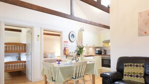 A cozy living room with a dining area, wooden floors, and a black leather sofa. - Willow Cottage,, Experience the North Downs in fully accessible comfort. (maidstone)