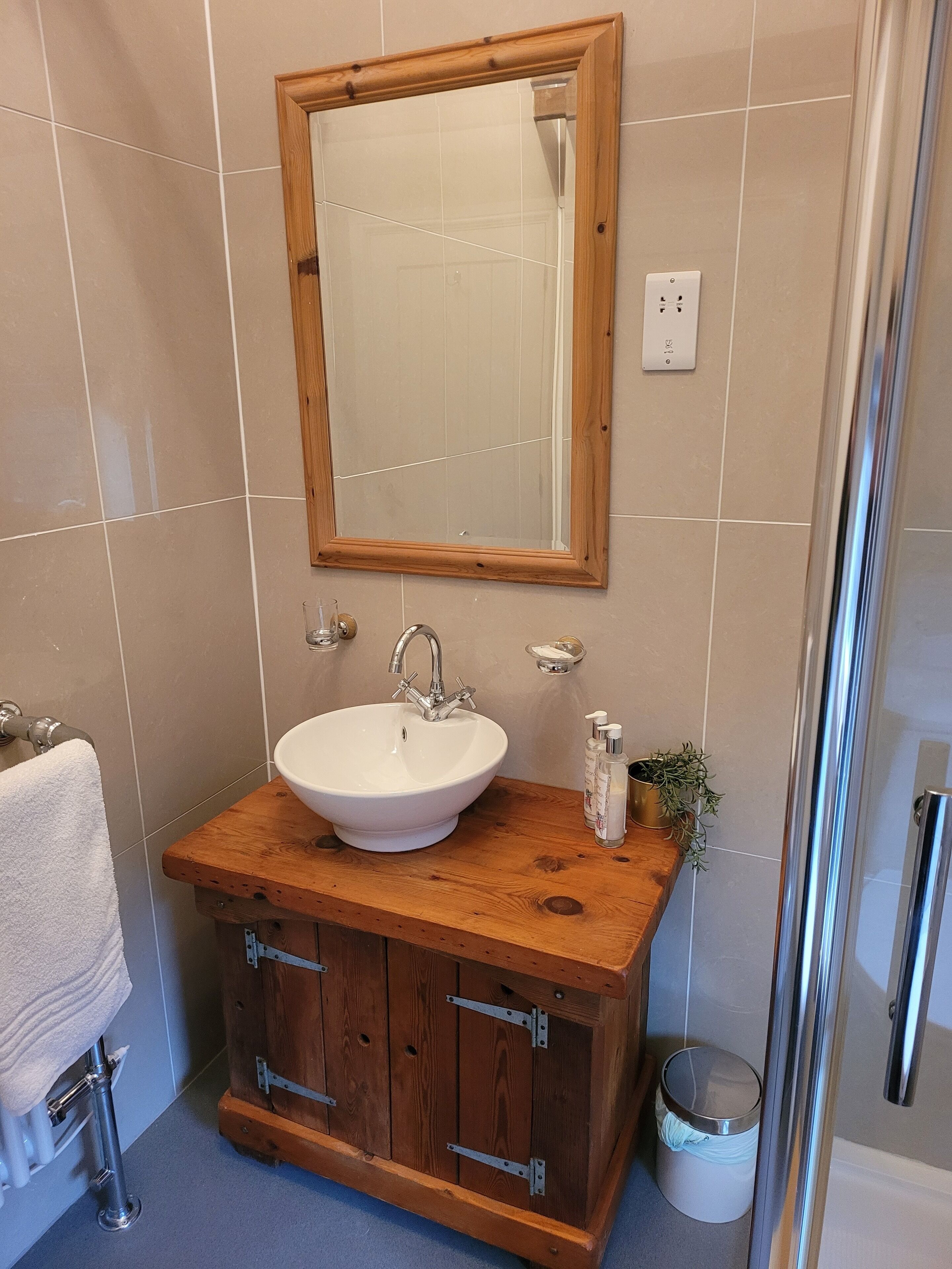 A bathroom with a wooden vanity, white sink, and a mirror above it.