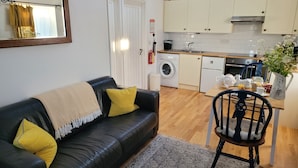 Una sala de estar con un sofá de cuero negro, un tapete estampado y un comedor con una mesa y sillas de madera.