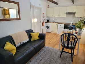 Een woonkamer met een zwarte leren bank, een kamerbreed tapijt met dessin, en een eethoek met een houten tafel en stoelen.