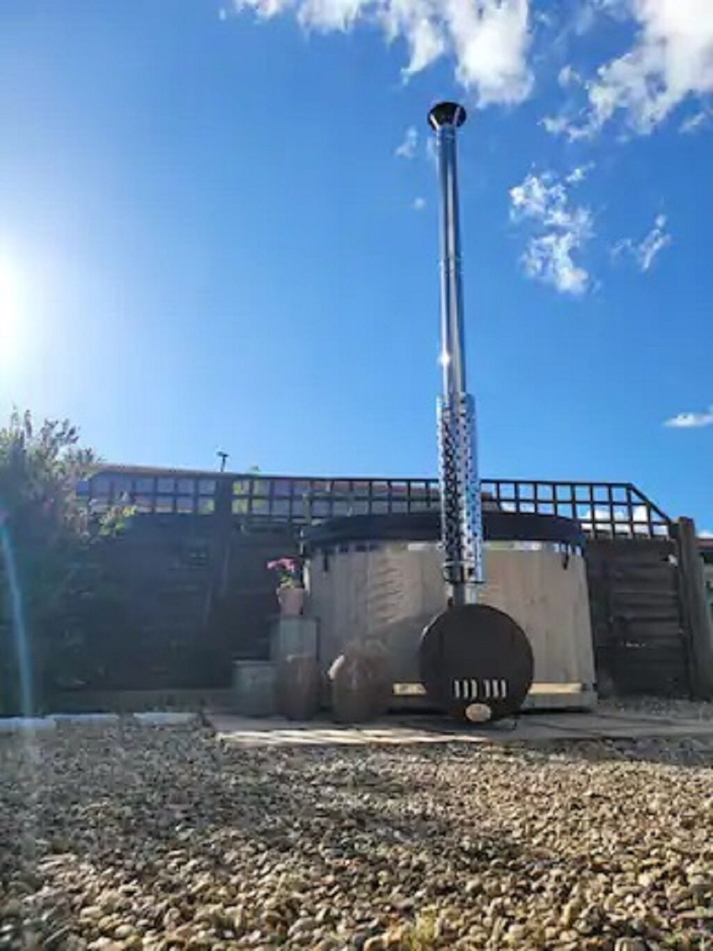 Une cheminée surmontée d’une grille métallique, un grand récipient en métal et un sol recouvert de gravier.
